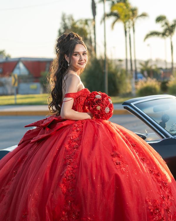 Quinceañera con vestido rojo junto a un auto clásico